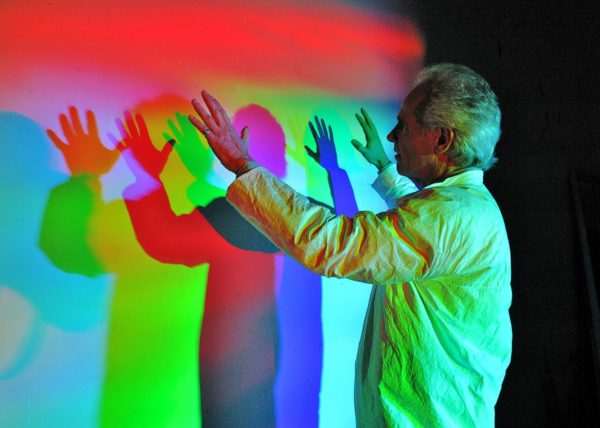 Man making multiple colored rainbow shadows of himself on a screen