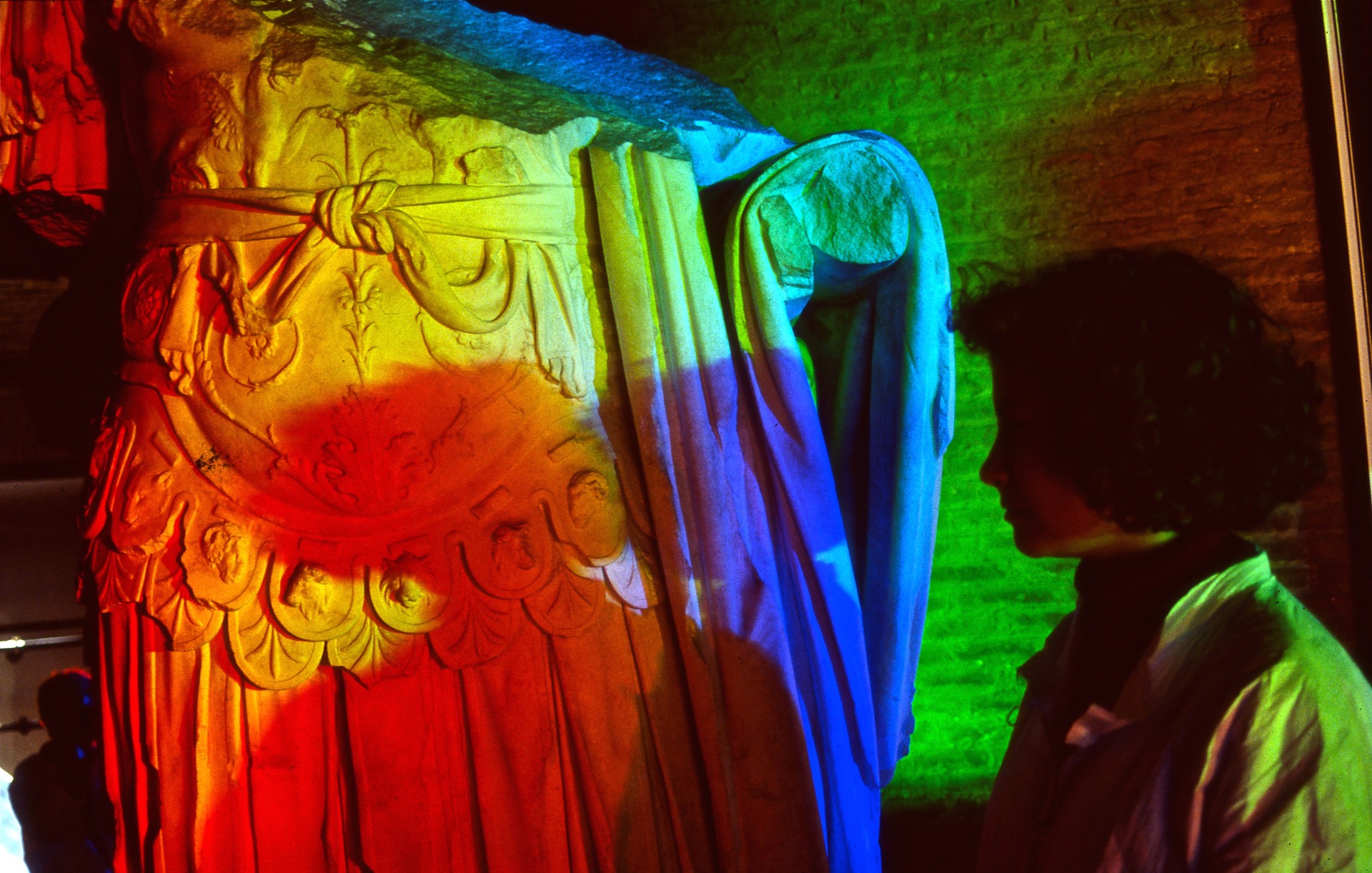 woman creates multiple colored solar spectrum shadows on an ancient Roman marble sculpture
